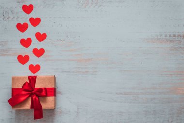Paper hearts and a craft present with red ribbon on a light painted wooden background. Top side angle view, flat lay. Valentines day concept. Copyspace.