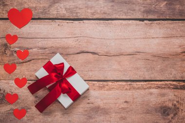 Paper hearts and a white present with red ribbon on a wooden background. Top side angle view, flat lay. Valentines day concept. Copyspace.