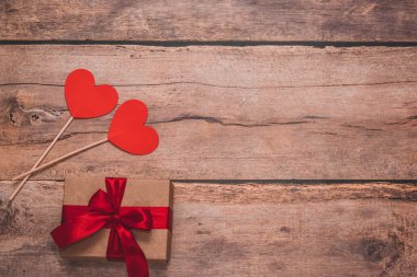 Paper hearts and a craft present with red ribbon on a wooden background. Top side angle view, flat lay. Valentines day concept. Copyspace.