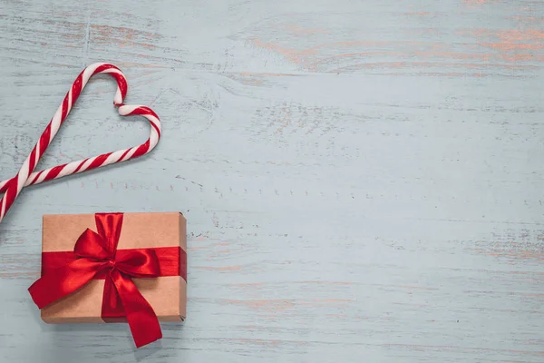 Sweets in hartvorm en een ambacht aanwezig met rood lint op een licht geschilderde houten achtergrond. Bovenste zijaanzicht, vlakke lay. Valentijnsdag concept. Kopieerruimte. — Stockfoto