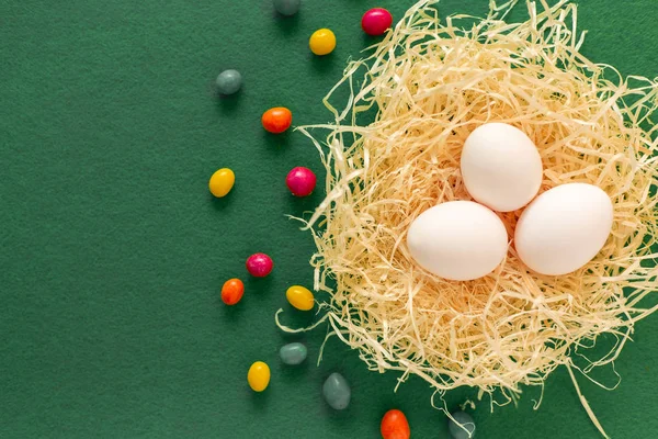 Três ovos em um ninho de feno e doces ao redor no fundo verde. Caraças! Copyspace para a redação. Conceito feriados Páscoa . — Fotografia de Stock