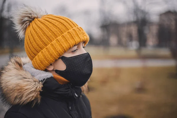 Jonge jongen met zwart medisch masker en oranje hoed. Coronavirus is een virus dat endemisch is in China. Bescherming tegen de ziekte voor kinderen. Gezondheidsveiligheidsconcept. — Stockfoto