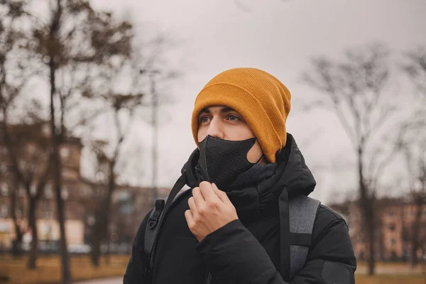 Un homme au chapeau orange enlève un masque médical noir dans la rue. Le coronavirus est un virus endémique en Chine. Protection contre la maladie pour les enfants. Concept de sécurité sanitaire . — Photo