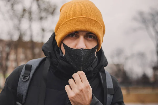 Man in orange hat takes off black medical mask on the street. Coronavirus is a virus that is endemic in China. Protection from the illness for children. Health safety concept. — Stock Photo, Image