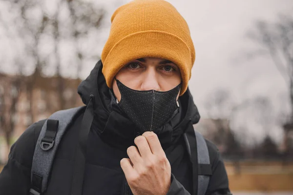 Mann mit orangefarbenem Hut zieht schwarze Arztmaske auf der Straße aus. Coronavirus ist ein Virus, das in China endemisch ist. Schutz vor der Krankheit für Kinder. Gesundheitssicherheitskonzept. — Stockfoto