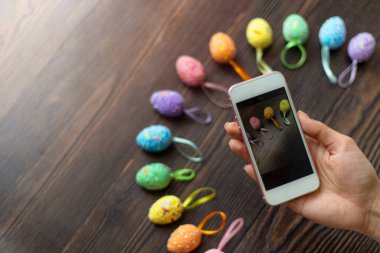 Kadın cep telefonuyla renkli paskalya yumurtalarının fotoğrafını çekiyor. Cep telefonu fotoğrafı. Metin ve sözcükler için metin alanı ve yer. Paskalya konsepti