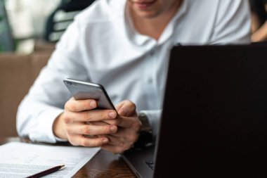 Laptop ve belgelerle dolu bir kafede beyaz bir moda gömleği ve cep telefonu giyen genç işadamlarının elleri. Serbest meslek ve serbest meslek kavramı. Uzaklık işi