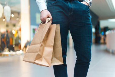 Alışveriş merkezinde elinde malzeme ve kıyafetlerle ekoloji dostu alışveriş çantalarıyla dolaşan şık bir genç adam. Satışlar, indirim konsepti. Mevsimlik satışlar