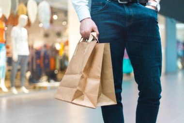 Alışveriş merkezinde elinde malzeme ve kıyafetlerle ekoloji dostu alışveriş çantalarıyla dolaşan şık bir genç adam. Satışlar, indirim konsepti. Mevsimlik satışlar