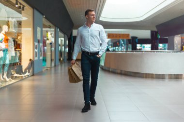Alışveriş merkezinde elinde malzeme ve kıyafetlerle ekoloji dostu alışveriş çantalarıyla gezen şık bir genç. Satışlar, indirim konsepti. Mevsimlik satışlar