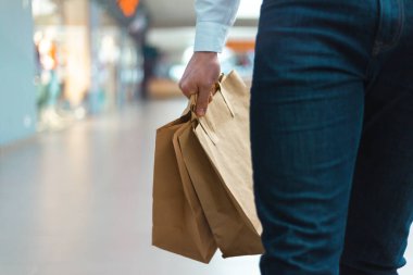 Alışveriş merkezinde elinde malzeme ve kıyafetlerle ekoloji dostu alışveriş çantalarıyla dolaşan şık bir genç adam. Satışlar, indirim konsepti. Mevsimlik satışlar