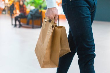 Alışveriş merkezinde elinde malzeme ve kıyafetlerle ekoloji dostu alışveriş çantalarıyla dolaşan şık bir genç adam. Satışlar, indirim konsepti. Mevsimlik satışlar