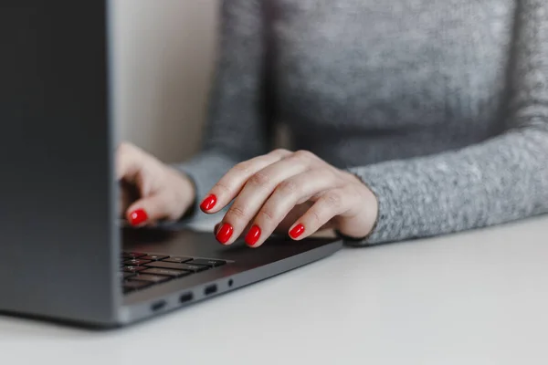 Closeup of woman's hands with red nails on the grey laptop keyboard. Young businesswoman working in an office on a computer. Business, industry and job concept