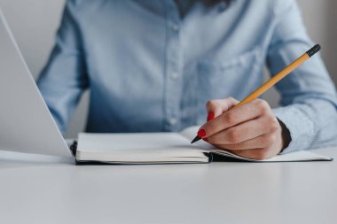 Bir not defterine sarı kalemle yazı yazan ve elinde belgeler tutan bir kadının el resmi. İş, serbest meslek ve serbest meslek. Uzaklık işi ve çevrimiçi iş kavramı