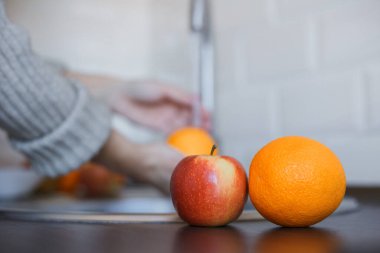 Genç bir kadın koronavirüs enfeksiyonunu önlemek için meyveleri yıkıyor. Portakal ve elma hijyeni korumak için iyice yıkanıyor. Virüs güvenliği. Covid-19 stop konsepti.