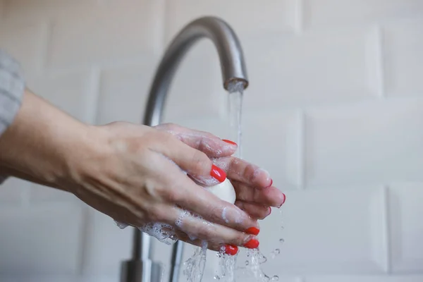 Крупный план молодой женщины моет руки с мылом, чтобы предотвратить коронавирусную инфекцию. Руки с красными ногтями тщательно промываются для поддержания гигиены. Безопасность вирусов. Ковид-19 . — стоковое фото