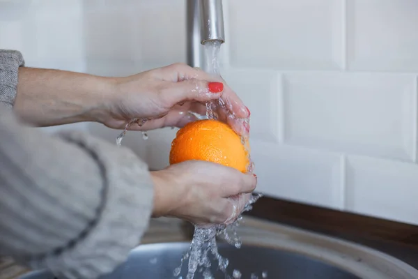 Крупный план молодой женщины моет фрукты, чтобы предотвратить коронавирусную инфекцию. Оранжевый тщательно промывают для поддержания гигиены. Безопасность вирусов. Ковид-19 . — стоковое фото