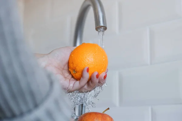 Крупный план молодой женщины моет фрукты, чтобы предотвратить коронавирусную инфекцию. Апельсин и яблоко тщательно промывают для поддержания гигиены. Безопасность вирусов. Ковид-19 . — стоковое фото