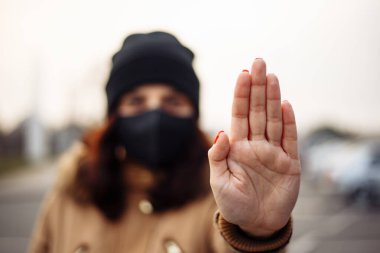 Siyah steril tıbbi maske takan genç bir kadın. Kız, nCov 2019 'u önlemek için el duruşu işareti gösteriyor. Karantina COVID-19 pandemik koronavirüs salgını ve sağlık konsepti