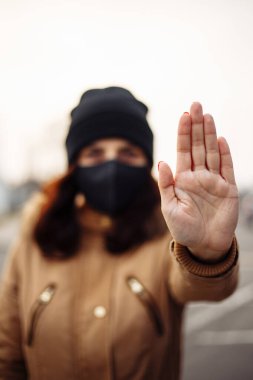 Siyah steril tıbbi maske takan genç bir kadın. Kız, nCov 2019 'u önlemek için el duruşu işareti gösteriyor. Karantina COVID-19 pandemik koronavirüs salgını ve sağlık konsepti