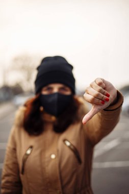 Siyah steril tıbbi maske takan genç bir kadın. Kız, nCov 2019 'u önlemek için hoşnutsuzluk işareti gösteriyor. Karantina COVID-19 pandemik koronavirüs salgını ve sağlık konsepti