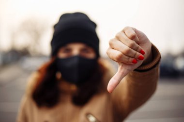 Kız, nCov 2019 'u önlemek için hoşnutsuzluk işareti gösteriyor. Siyah steril tıbbi maske takan genç bir kadın. Karantina COVID-19 pandemik koronavirüs salgını ve sağlık konsepti