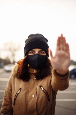 Kızım, yüzünde koruyucu steril tıbbi siyah maske takan genç bir kadın dışarıdaki kameralara bakıyor, şehir sokaklarında avuç içi, el, dur işareti yok. Kirlilik, virüs, pandemik koronavirüs konsepti