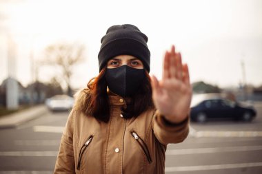 Kızım, yüzünde koruyucu steril tıbbi siyah maske takan genç bir kadın dışarıdaki kameralara bakıyor, şehir sokaklarında avuç içi, el, dur işareti yok. Kirlilik, virüs, pandemik koronavirüs konsepti