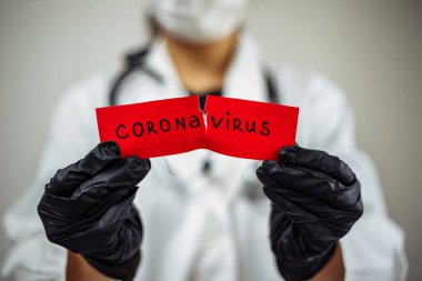 Cerrahi maskeli doktor kadın gri arka planda izole edilmiş kırmızı bir kağıdı kurtarıcı Coronavirüs ile yırtıyor. Kadın hemşire nCov2019 işareti taşıyor. Covid-19 ve hastalık önleme konsepti