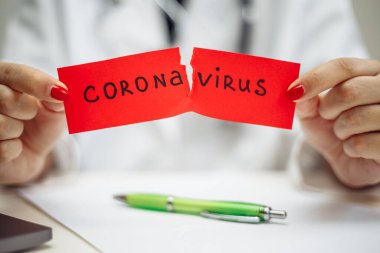 Cerrahi maskeli doktor kadın gri arka planda izole edilmiş kırmızı bir kağıdı kurtarıcı Coronavirüs ile yırtıyor. Kadın hemşire nCov2019 işareti taşıyor. Covid-19 ve hastalık önleme konsepti