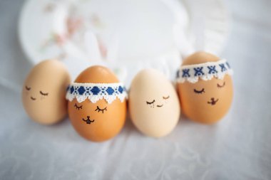 Üzerinde boyanmış tavşan yüzleri ve kulakları olan dört küçük paskalya yumurtası masanın üzerinde izole bir şekilde duruyor. Paskalya tatili süslemeleri ve hazırlık konsepti. Kutsal Din Günü