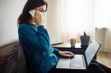 İş kadını evde kalır ve koronavirüs epidemisi karantinasında çalışır. Tıbbi maske takan, dizüstü bilgisayarda yazan, cep telefonuyla konuşan bir kadın işçi. Covid-19 pandemisi yayılma önleyici
