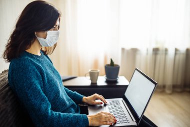 İş kadını evde kalır ve koronavirüs epidemisi karantinasında çalışır. Tıbbi maske takan ve dizüstü bilgisayarda yazan bir kadın işçi. Covid-19 pandemisi yayılma önleme kavramı