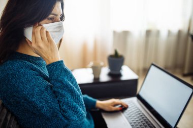 İş kadını evde kalır ve koronavirüs epidemisi karantinasında çalışır. Tıbbi maske takan, dizüstü bilgisayarda yazan, cep telefonuyla konuşan bir kadın işçi. Covid-19 pandemisi yayılma önleyici