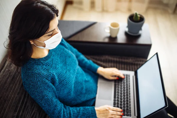 İş kadını evde kalır ve koronavirüs epidemisi karantinasında çalışır. Tıbbi maske takan ve dizüstü bilgisayarda yazan bir kadın işçi. Covid-19 pandemisi yayılma önleme kavramı
