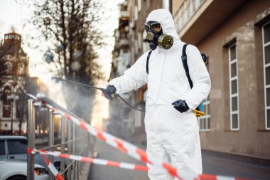 Koruyucu ekipman kullanan bir adam şehirde dezenfektanla dezenfekte ediyor. Coronavirus covid-19 hastalığından dolayı yüzey tedavisi. Beyaz takım elbiseli bir adam sokakları ve rayları dezenfekte ediyor. Virüs salgını