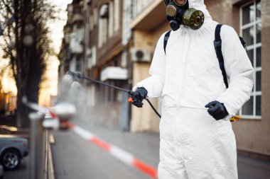 Koruyucu ekipman kullanan bir adam şehirde dezenfektanla dezenfekte ediyor. Coronavirus covid-19 hastalığından dolayı yüzey tedavisi. Beyaz takım elbiseli bir adam sokakları ve rayları dezenfekte ediyor. Virüs salgını