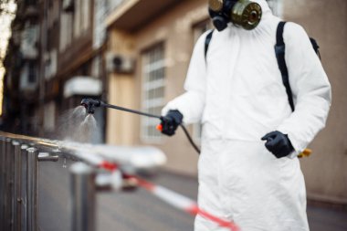 Koruyucu ekipman kullanan bir adam şehirde dezenfektanla dezenfekte ediyor. Coronavirus covid-19 hastalığından dolayı yüzey tedavisi. Beyaz takım elbiseli bir adam sokakları ve rayları dezenfekte ediyor. Virüs salgını