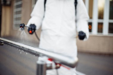 Koruyucu ekipman kullanan bir adam şehirde dezenfektanla dezenfekte ediyor. Coronavirus covid-19 hastalığından dolayı yüzey tedavisi. Beyaz takım elbiseli bir adam sokakları ve rayları dezenfekte ediyor. Virüs salgını