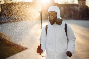 A man in a protective disinfection suit sprays sterilizer on the park square to prevent spread of coronavirus covid-19. Professional saniraty worker cleans city streets from the virus. Spot nCov2019 clipart