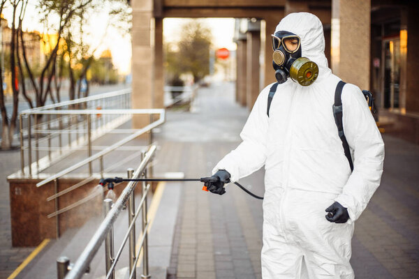 Мужчина дезинфицирует перила в защитном костюме и снаряжении от коронавируса. Очистка и стерилизация не переполненных городских улиц. Предотвращение распространения вируса Covid-19
