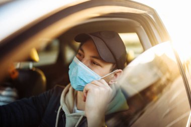 Koronavirüs salgını karantinası sırasında bir çocuk araba kullanıyor ve steril maske takıyor. Trafik sıkışıklığında bekleyen bir adam umut arıyor. Virüsün kendini koruma yoluyla yayılmasını engelle