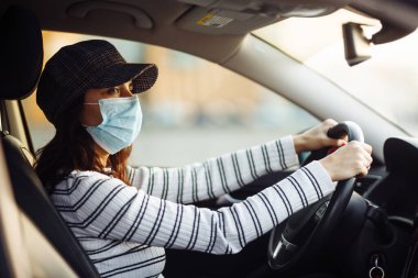 Kadın araba sürücüsü salgın koronavirüs karantinası sırasında steril maske takıyor. Covid-19 virüsünün yayılmasını engellemek için izolasyon taşıyın. Sağlık hizmetleri kavramı