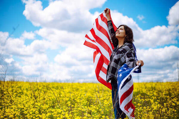 Patriotic young woman wrapped in an american flag on a beautiful field with yellow flowers. USA independence day 4th of July celebration. Summer holidays concept
