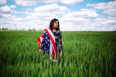 Genç bir kadın yeşil buğday tarlasında Amerikan bayrağı sallıyor. Vatansever bayram kutlaması. Amerika Birleşik Devletleri Bağımsızlık Günü, 4 Temmuz konsepti