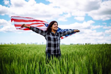 Genç bir kadın yeşil buğday tarlasında Amerikan bayrağı sallıyor. Vatansever bayram kutlaması. Amerika Birleşik Devletleri Bağımsızlık Günü, 4 Temmuz konsepti