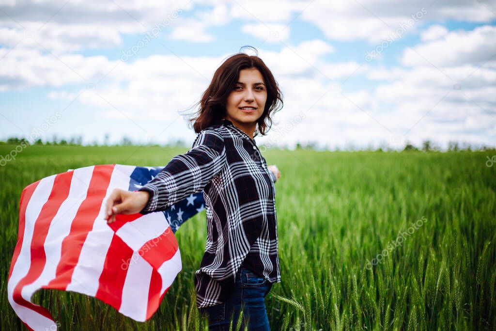 Young woman waves an american flag on the green wheat field. Patriotic holiday celebration. United States of America independence day, 4th of July concept