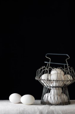 Beyaz yumurta dolu eski metal bir kupa, beyaz masa örtüsü ve siyah arka plan. Tavuk yumurtası. Kopyala, metin için boşluk.