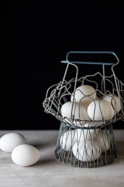 Beyaz yumurta dolu eski metal bir kupa, beyaz masa örtüsü ve siyah arka plan. Tavuk yumurtası. Kopyala, metin için boşluk.