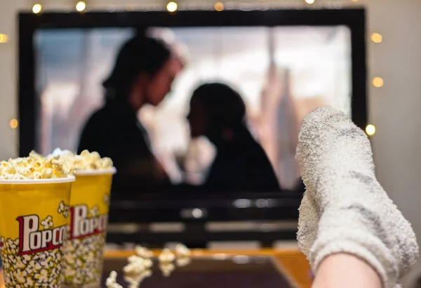 Young woman watching watching a movie with popcorn. Television (film) with feet on the table.